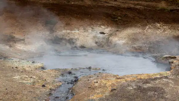 A huge puddle of mud is steaming strongly with yellow and orange rocks in the background